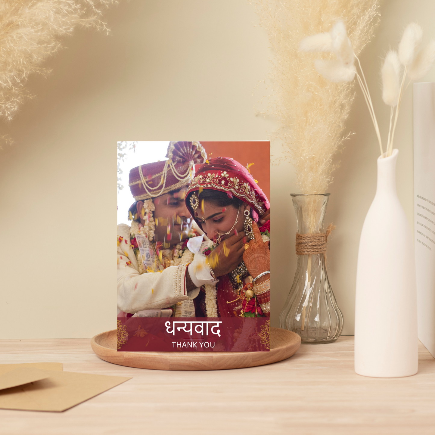 A wedding thank you card rests on a wooden plate. Various vases with pampas grass sit in the background.