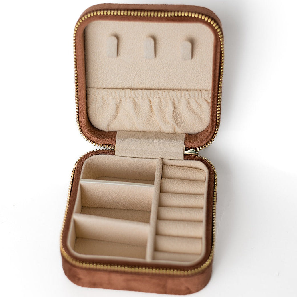 The inside of a chocolate-coloured jewelry case. There are three storage sections and seven ring slots on the bottom portion of the case. On the top half, there are three hooks for chains or necklaces and well as a pouch to tuck them in.