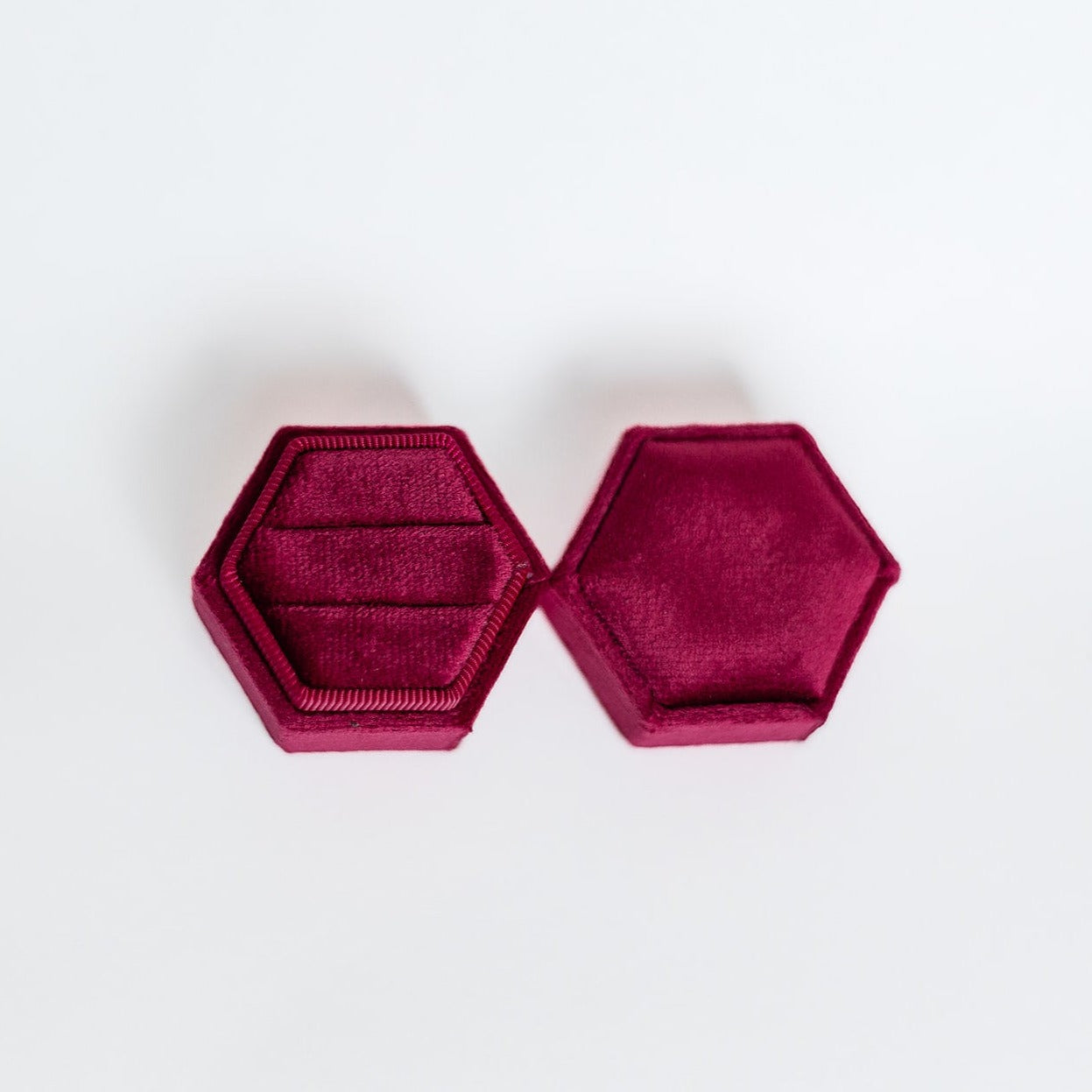 A raspberry hexagon ring box lays open displaying the two ring slots in the base.