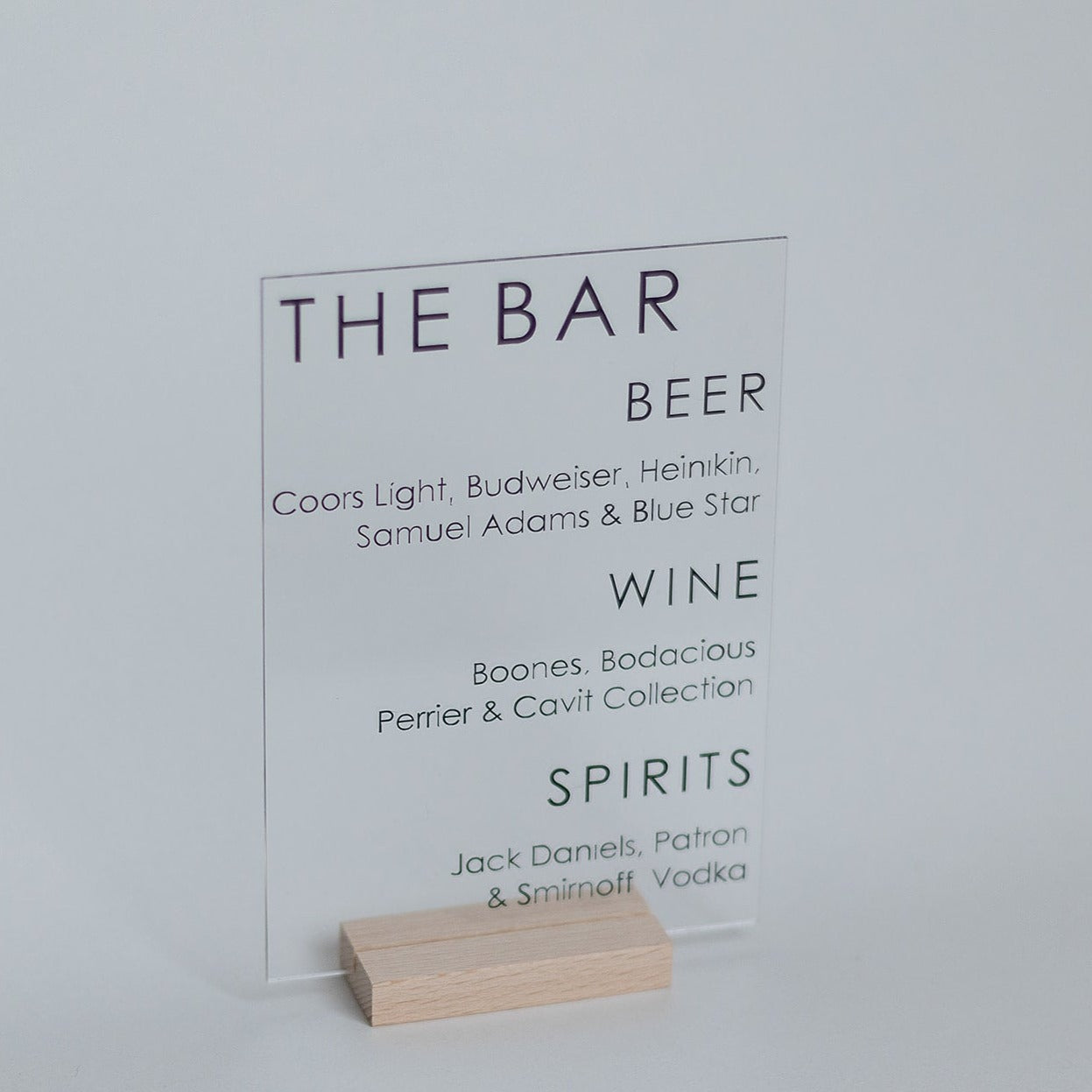 A small acrylic bar menu with black text on a light wood base.