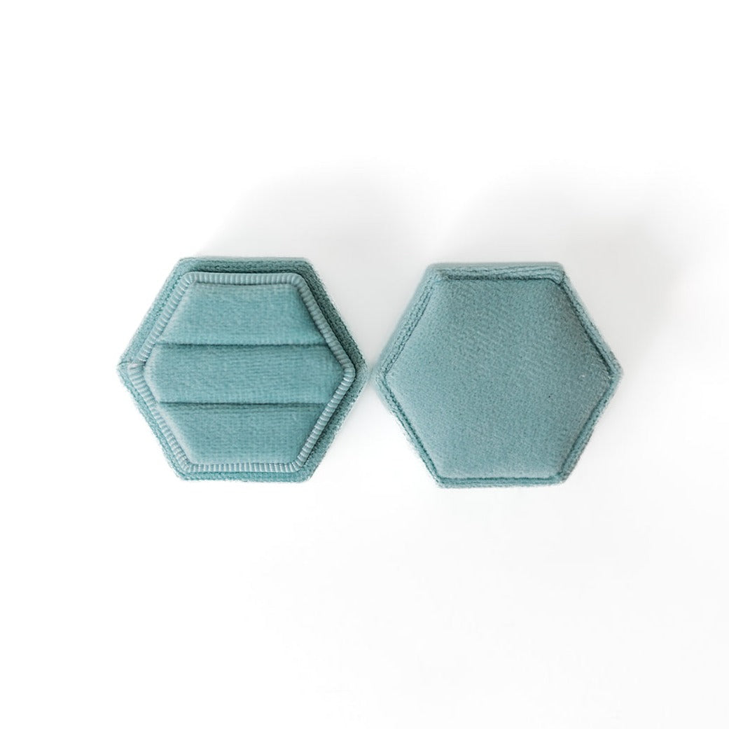 An aqua hexagon ring box lays open displaying the two ring slots in the base.