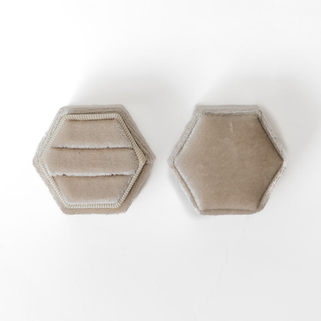 An ivory hexagon ring box lays open displaying the two ring slots in the base.