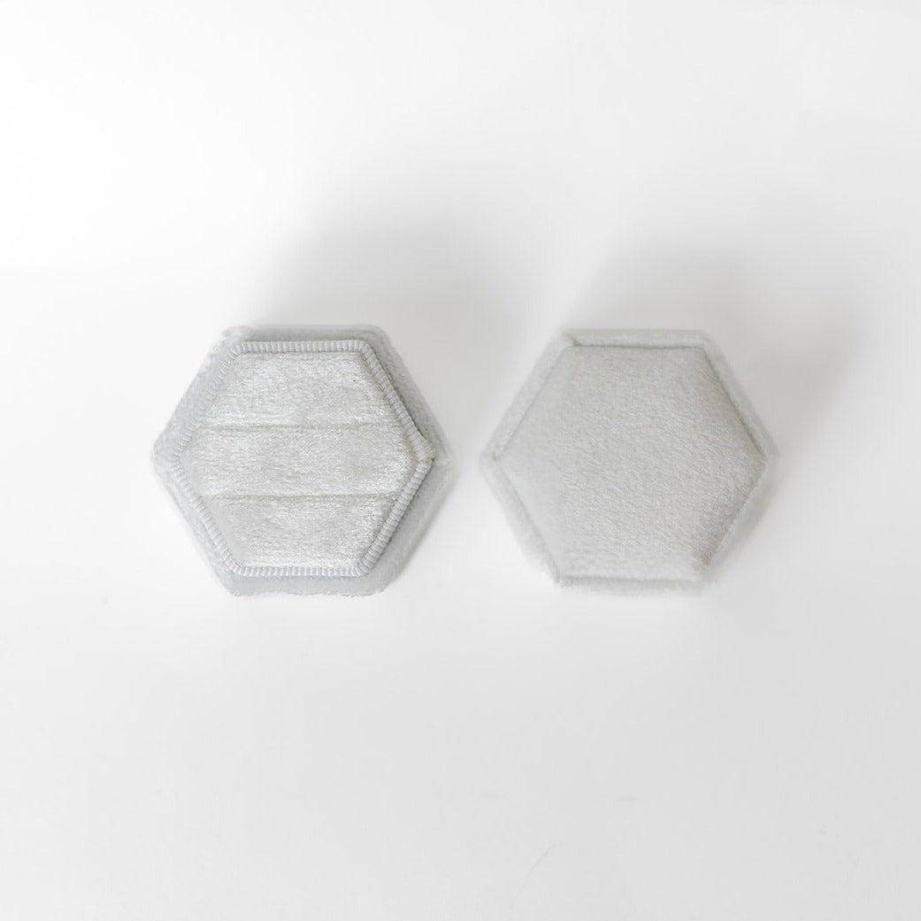 A white hexagon ring box lays open displaying the two ring slots in the base.
