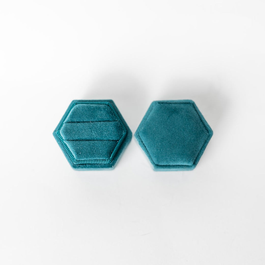 A teal hexagon ring box lays open displaying the two ring slots in the base.