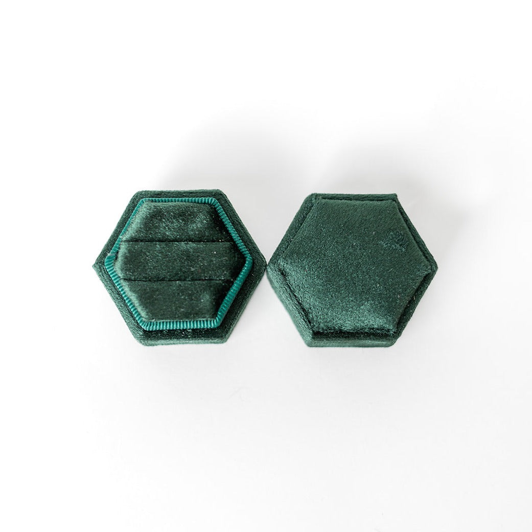 An emerald hexagon ring box lays open displaying the two ring slots in the base.