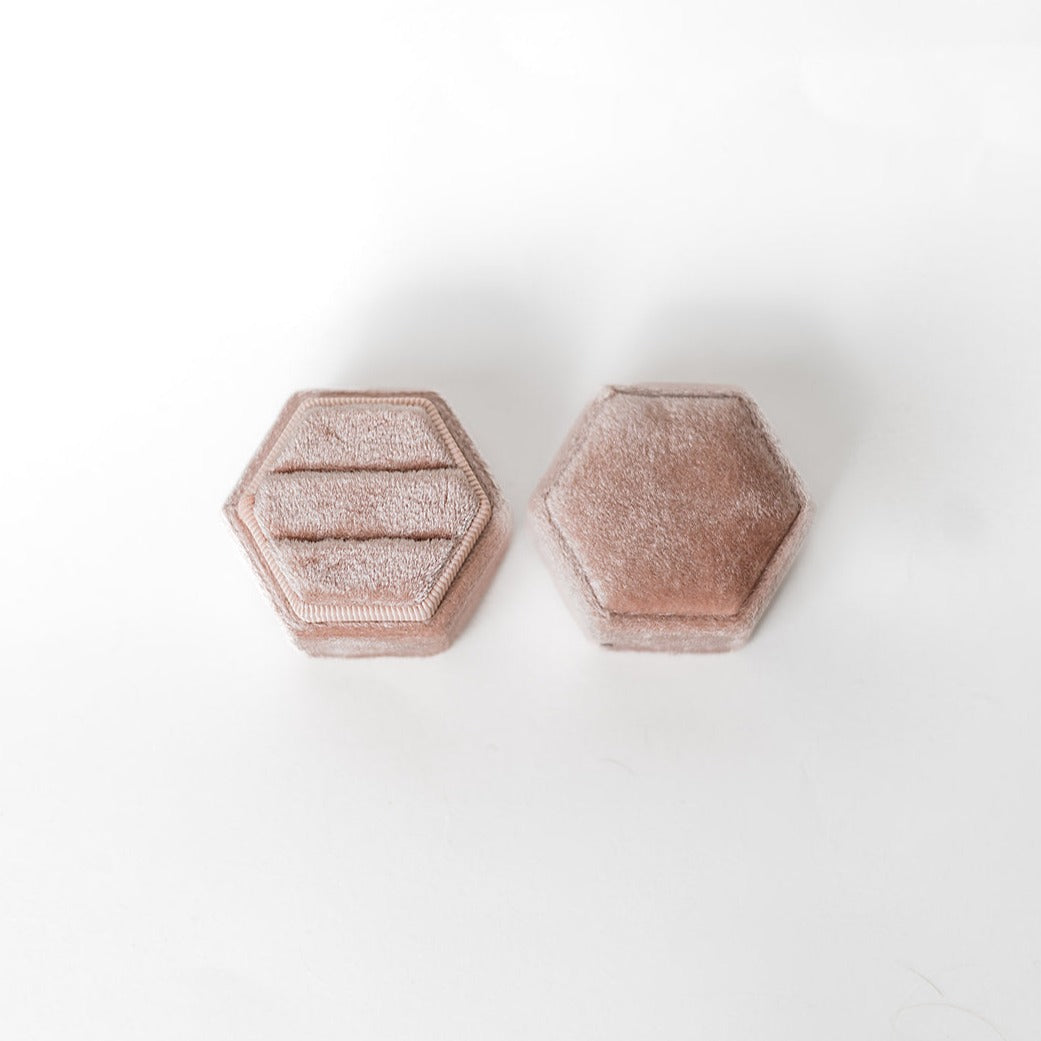 A blush-coloured hexagon ring box lays open displaying the two ring slots in the base.