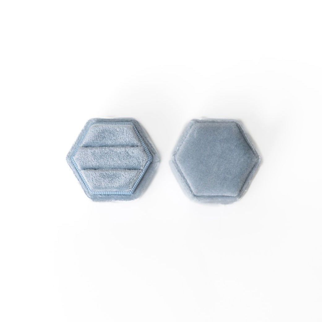 A powder blue hexagon ring box lays open displaying the two ring slots in the base.