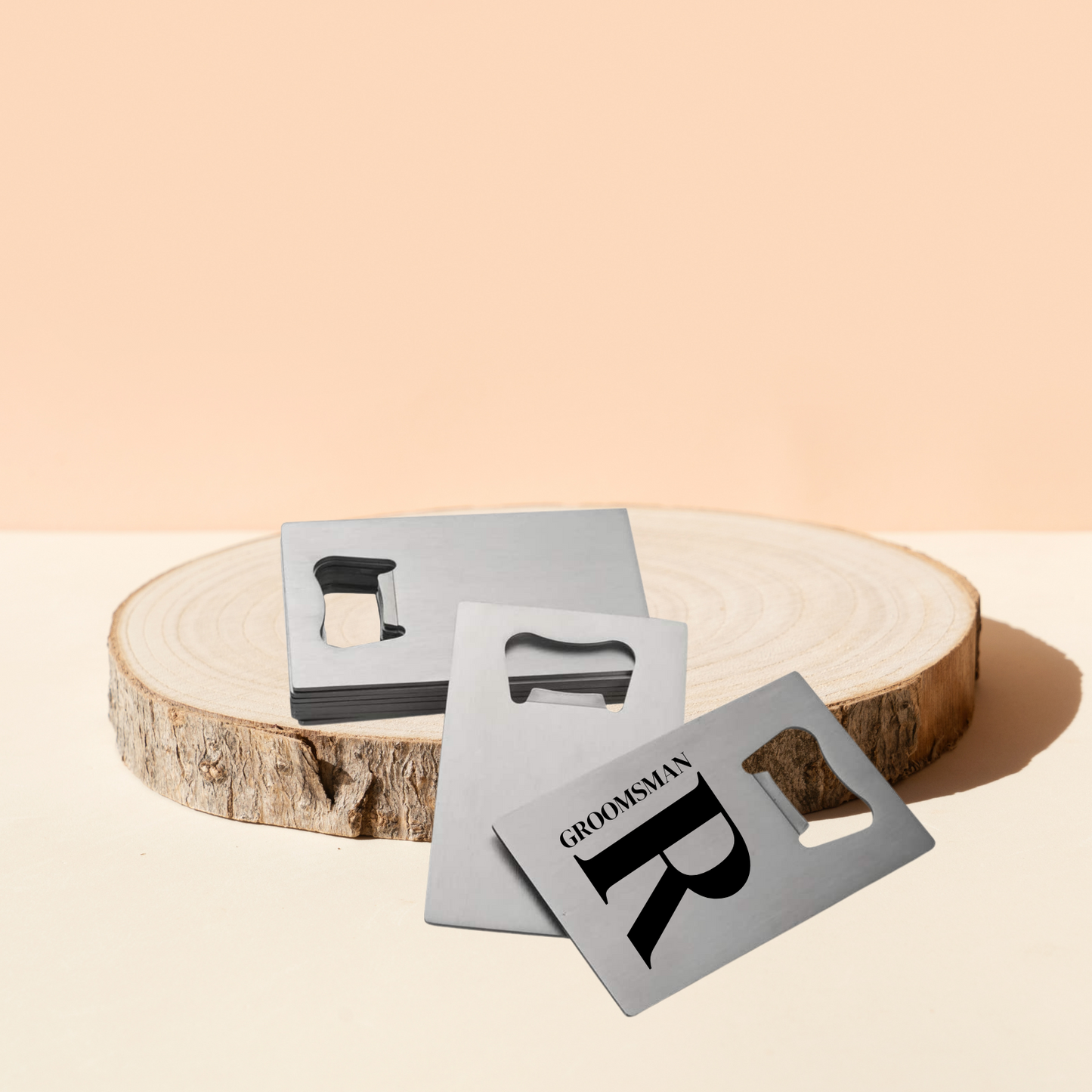 Stainless steel bottle openers are piled on a wooden round against a light coral-coloured background.