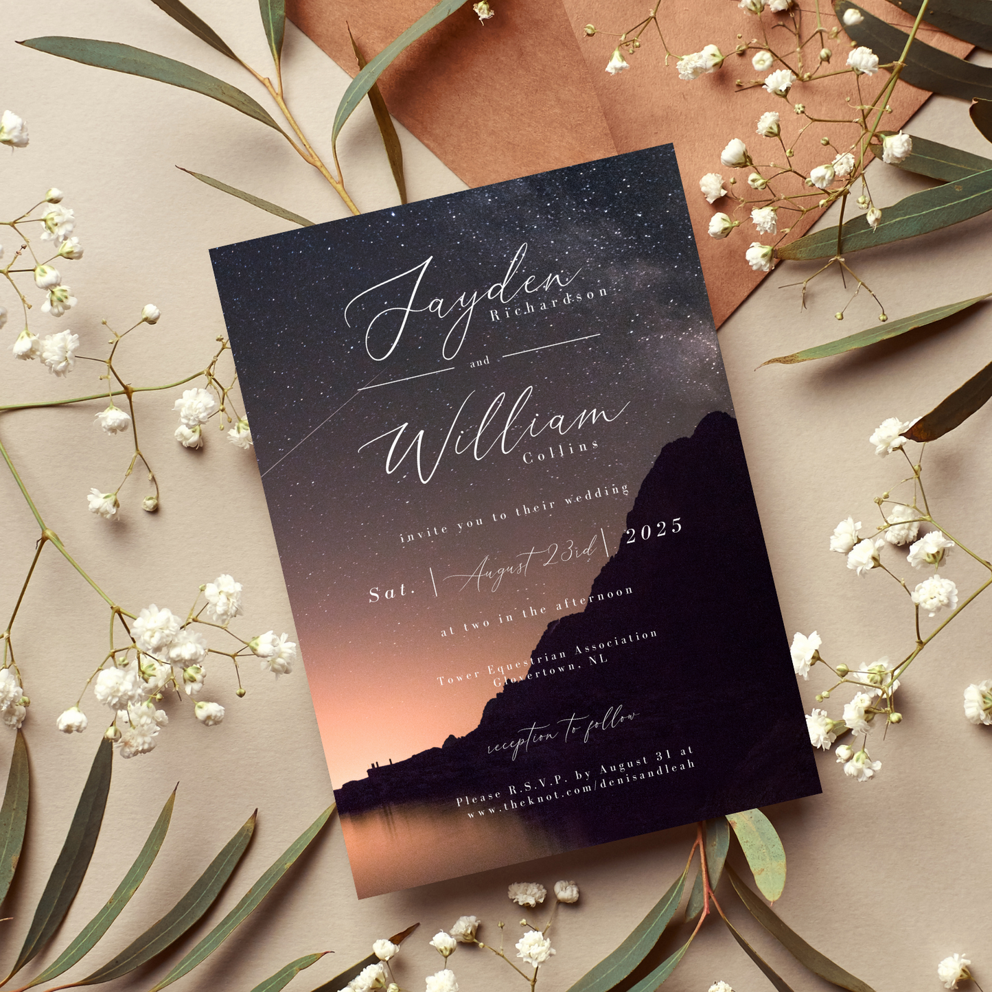 A wedding invitation that features a night time scene sits against a beige-coloured background. There are thin leaves and baby's breath surrounding the invitation.