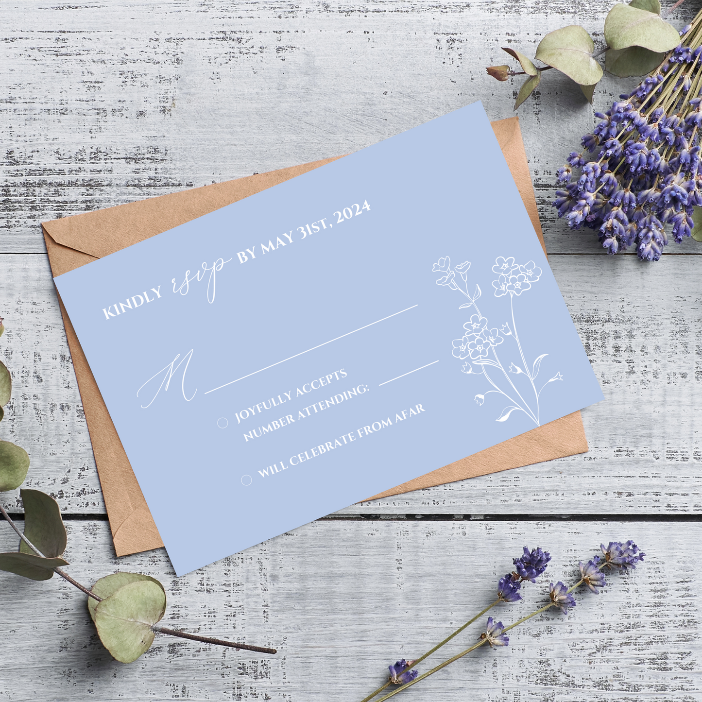 A light blue card sits on top of a kraft paper envelope against a rustic wood background. Sprigs of lilac and eucalyptus surround the card. On the R.S.V.P. itself, there is white text and a minimalist floral design.