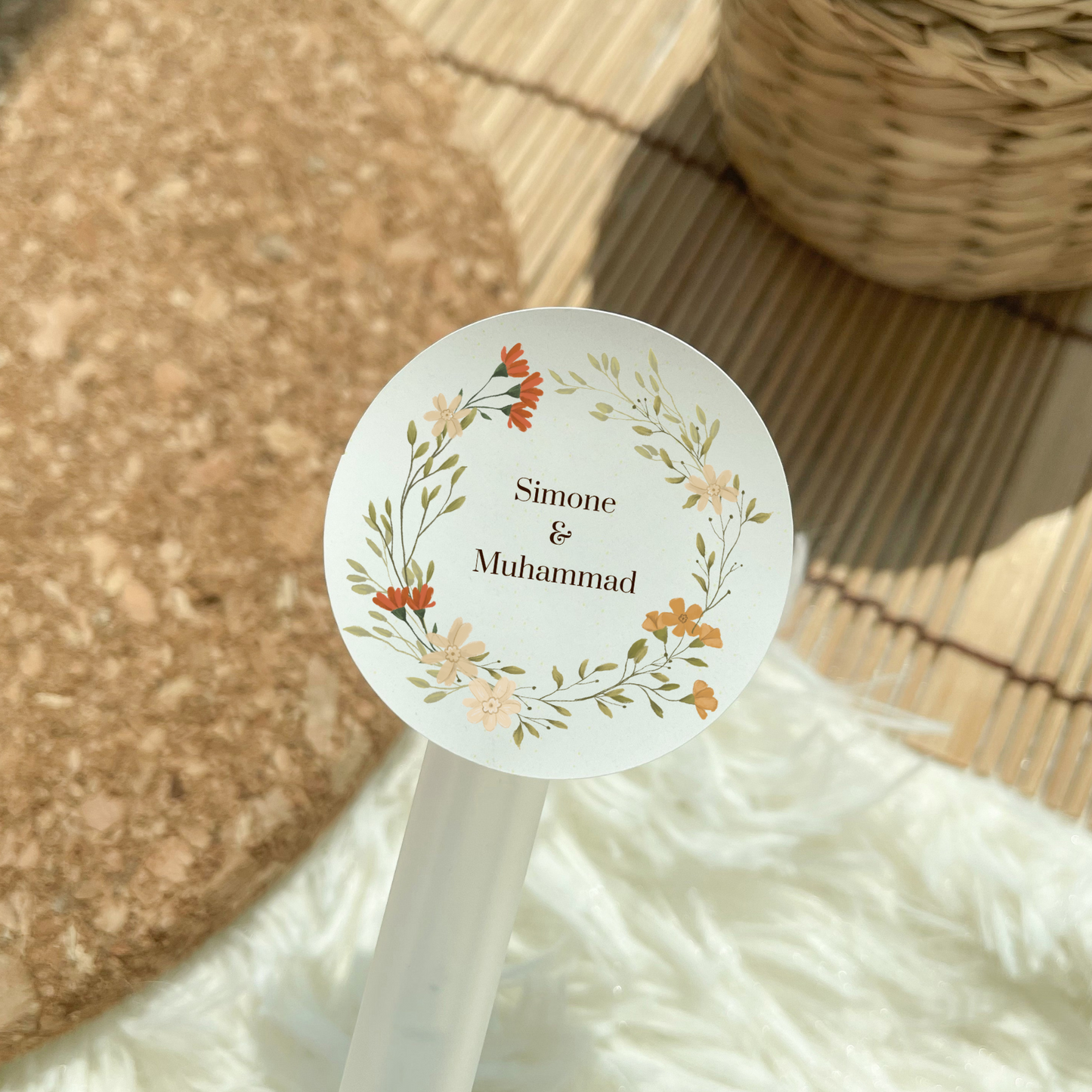A round sticker hovers above a bohemian style backdrop. The sticker says "Simone & Muhammad" and has a wreath of flowers around the text.