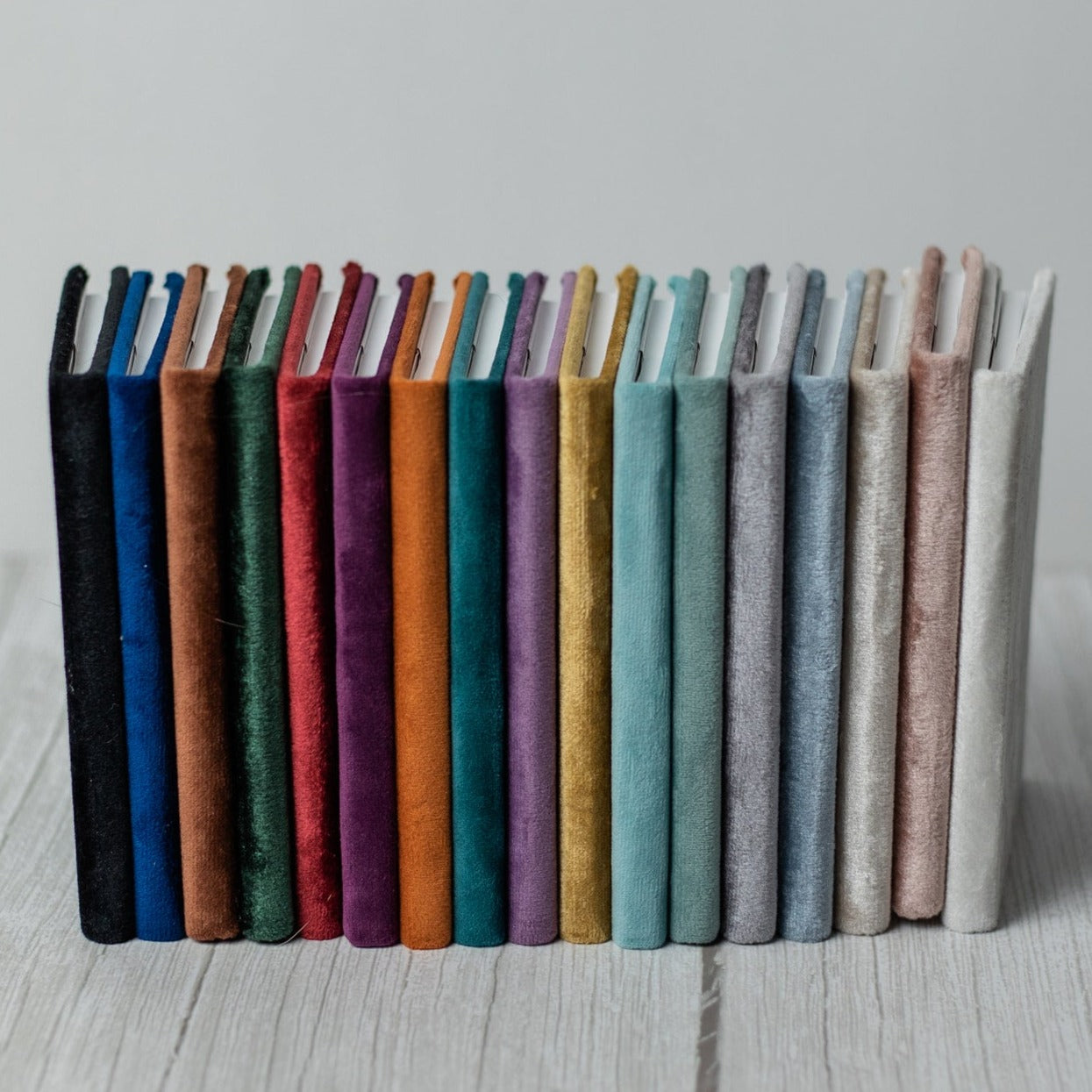 Multiple velvet vow books stand upright in a line from the darkest shade to the lightest.