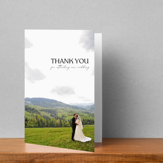 A wedding thank you card sits on a wooden table against a light grey background.