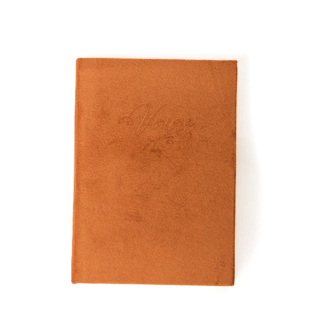 A burnt orange vow book with the word "Vows" embossed on the front cover.