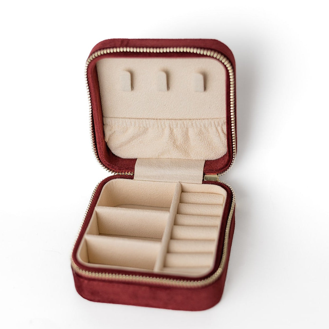 The inside of a merlot jewelry case. There are three storage sections and seven ring slots on the bottom portion of the case. On the top half, there are three hooks for chains or necklaces and well as a pouch to tuck them in.