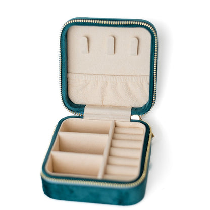 The inside of a teal jewelry case. There are three storage sections and seven ring slots on the bottom portion of the case. On the top half, there are three hooks for chains or necklaces and well as a pouch to tuck them in.