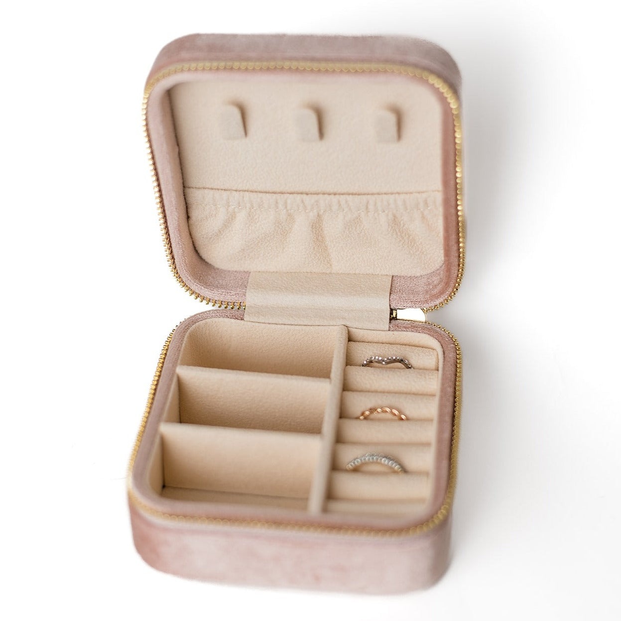 The inside of a blush-coloured jewelry case. There are three storage sections and seven ring slots on the bottom portion of the case. On the top half, there are three hooks for chains or necklaces and well as a pouch to tuck them in.