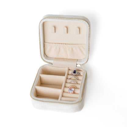 The inside of a white jewelry case. There are three storage sections and seven ring slots on the bottom portion of the case. On the top half, there are three hooks for chains or necklaces and well as a pouch to tuck them in.