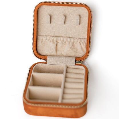 The inside of a burnt orange jewelry case. There are three storage sections and seven ring slots on the bottom portion of the case. On the top half, there are three hooks for chains or necklaces and well as a pouch to tuck them in.