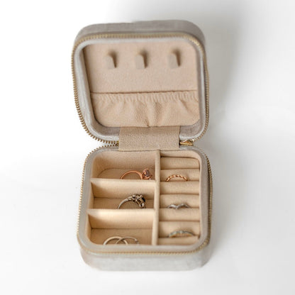 The inside of an ivory jewelry case. There are three storage sections and seven ring slots on the bottom portion of the case. On the top half, there are three hooks for chains or necklaces and well as a pouch to tuck them in.