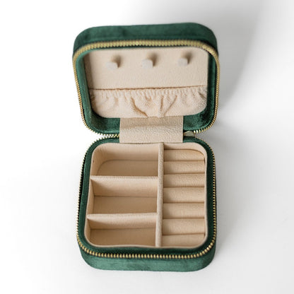 The inside of an emerald jewelry case. There are three storage sections and seven ring slots on the bottom portion of the case. On the top half, there are three hooks for chains or necklaces and well as a pouch to tuck them in.