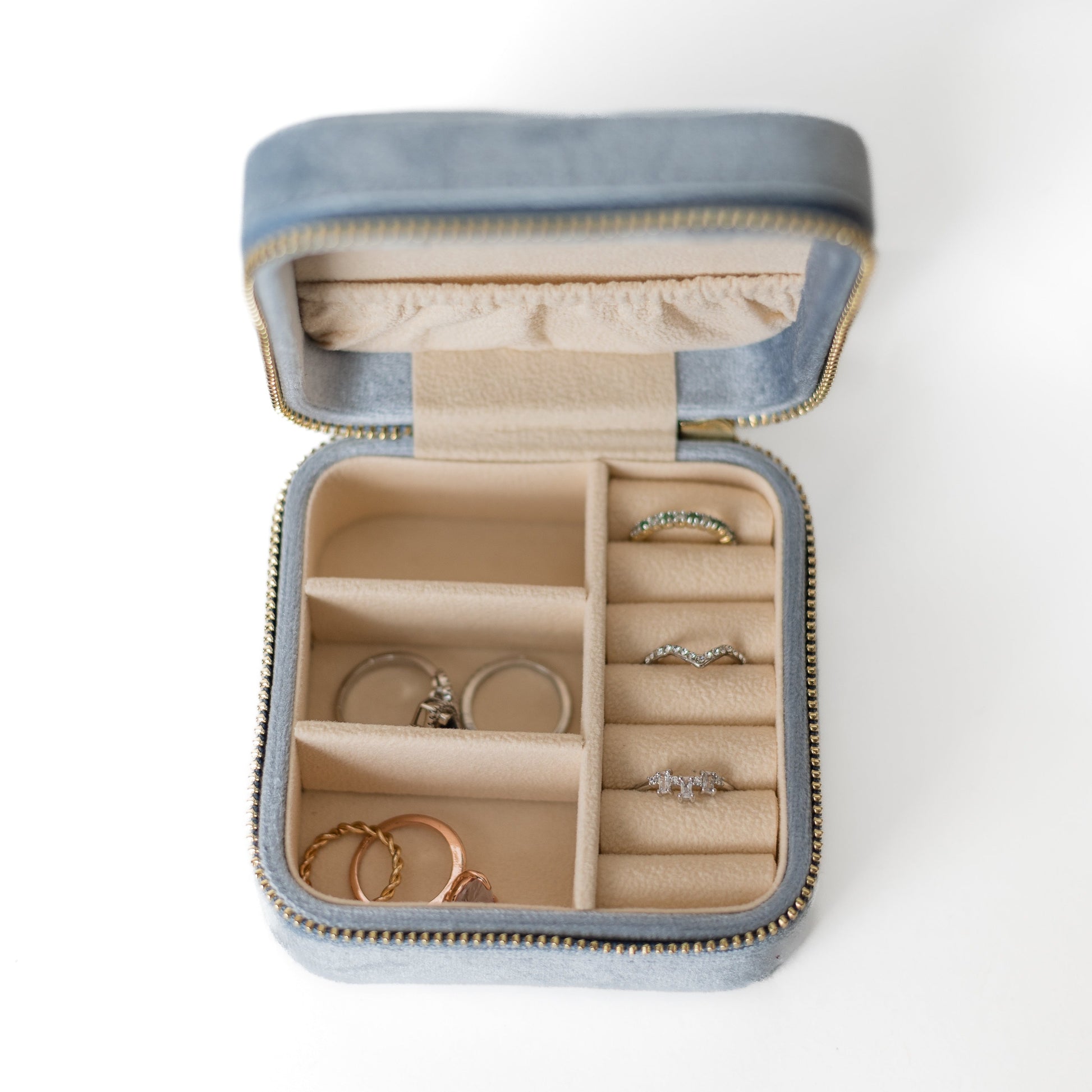 The inside of a powder blue jewelry case. There are three storage sections and seven ring slots on the bottom portion of the case. On the top half, there are three hooks for chains or necklaces and well as a pouch to tuck them in.