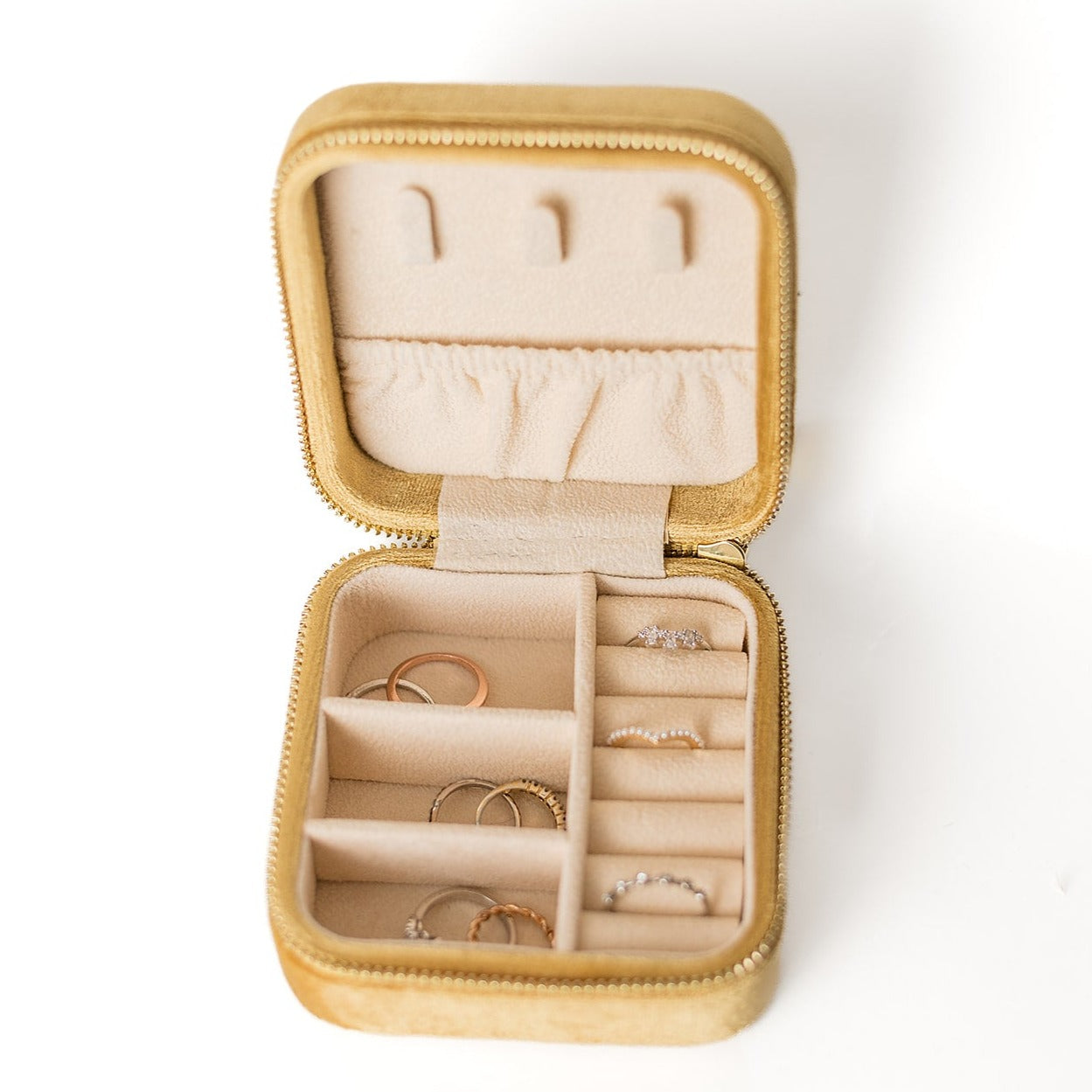 The inside of a mustard-coloured jewelry case. There are three storage sections and seven ring slots on the bottom portion of the case. On the top half, there are three hooks for chains or necklaces and well as a pouch to tuck them in.