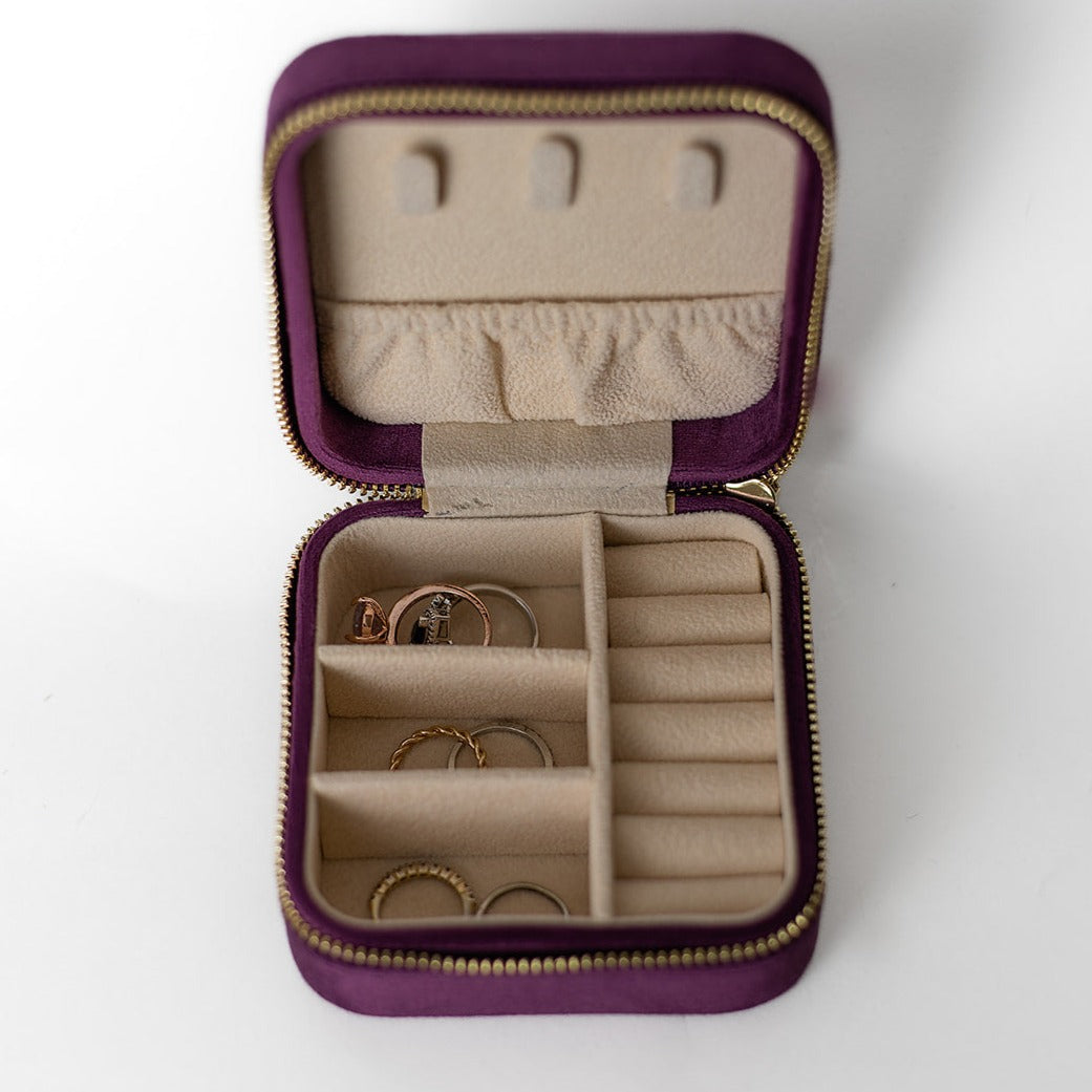 The inside of a plum-cloured jewelry case. There are three storage sections and seven ring slots on the bottom portion of the case. On the top half, there are three hooks for chains or necklaces and well as a pouch to tuck them in.