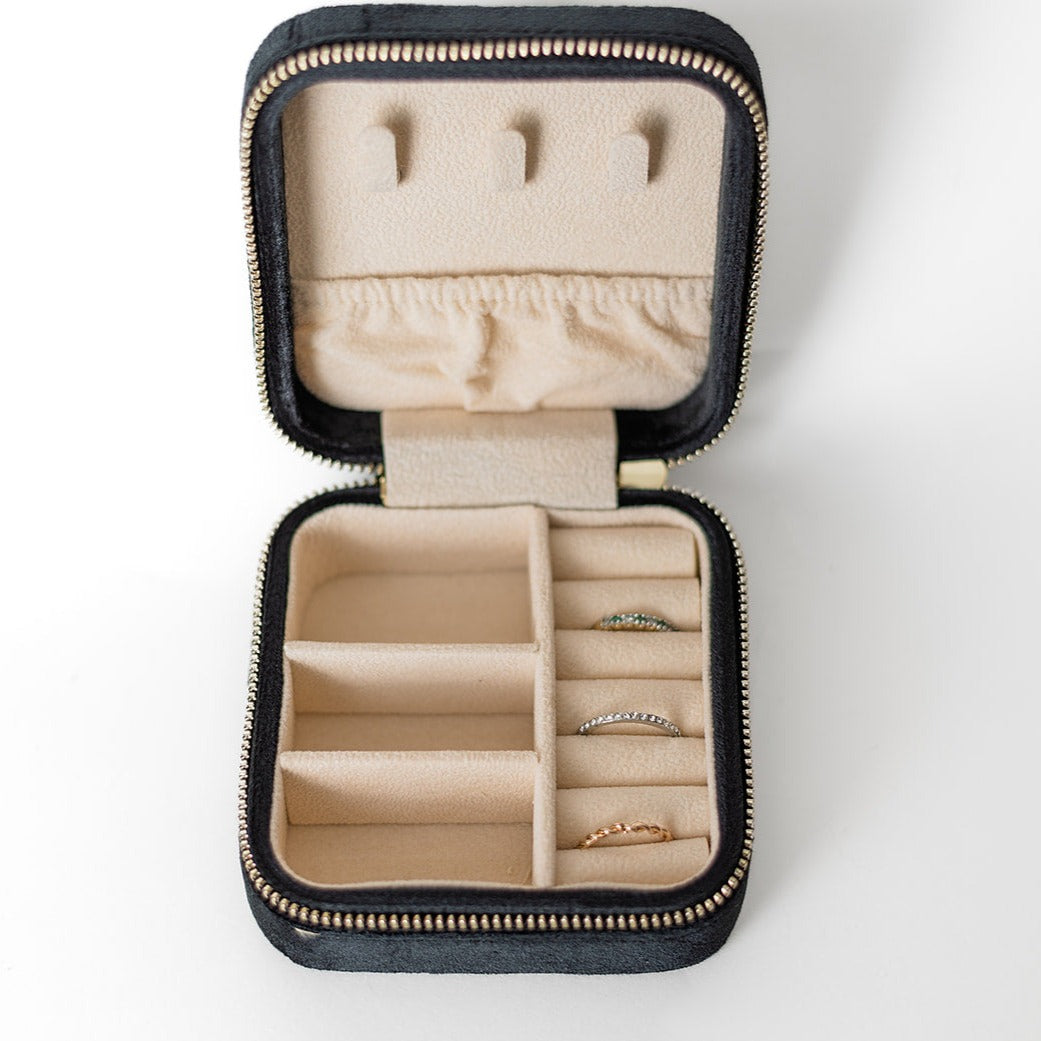 The inside of a black jewelry case. There are three storage sections and seven ring slots on the bottom portion of the case. On the top half, there are three hooks for chains or necklaces and well as a pouch to tuck them in.