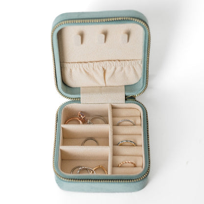 The inside of a sage jewelry case. There are three storage sections and seven ring slots on the bottom portion of the case. On the top half, there are three hooks for chains or necklaces and well as a pouch to tuck them in.
