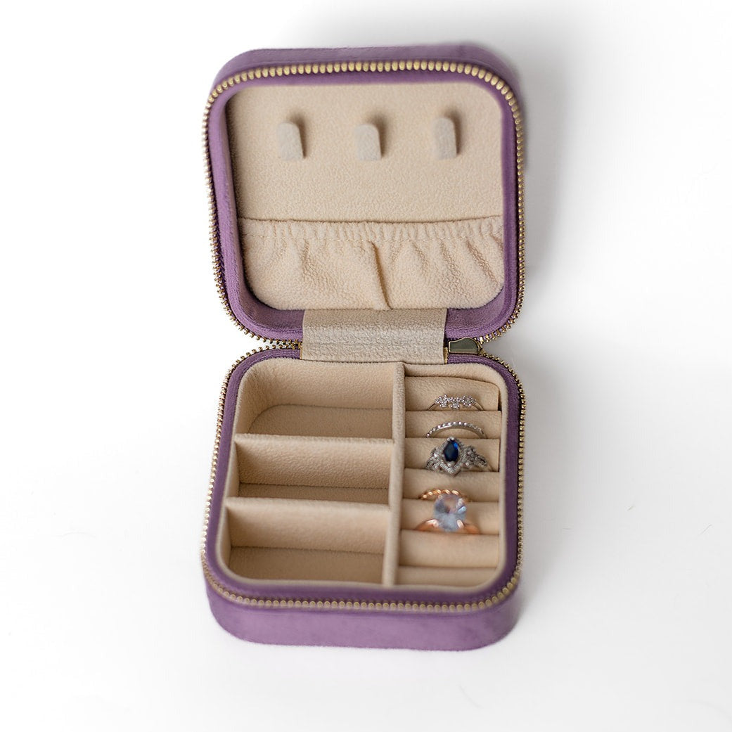The inside of a mauve jewelry case. There are three storage sections and seven ring slots on the bottom portion of the case. On the top half, there are three hooks for chains or necklaces and well as a pouch to tuck them in.