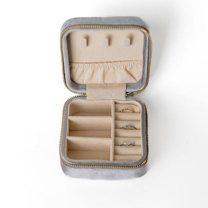 The inside of a silver jewelry case. There are three storage sections and seven ring slots on the bottom portion of the case. On the top half, there are three hooks for chains or necklaces and well as a pouch to tuck them in.