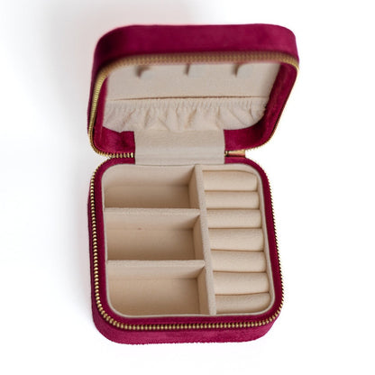 The inside of a raspberry-coloured jewelry case. There are three storage sections and seven ring slots on the bottom portion of the case. On the top half, there are three hooks for chains or necklaces and well as a pouch to tuck them in.