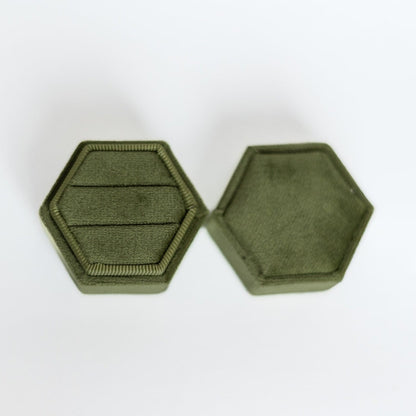 An olive-coloured hexagon ring box lays open displaying the two ring slots in the base.