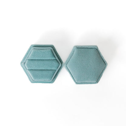 An aqua hexagon ring box lays open displaying the two ring slots in the base. 
