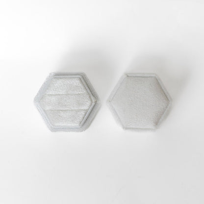 A white hexagon ring box lays open displaying the two ring slots in the base. 