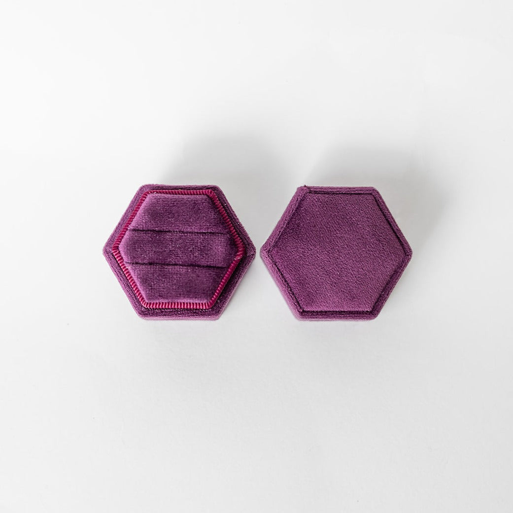 A plum-coloured hexagon ring box lays open displaying the two ring slots in the base. 