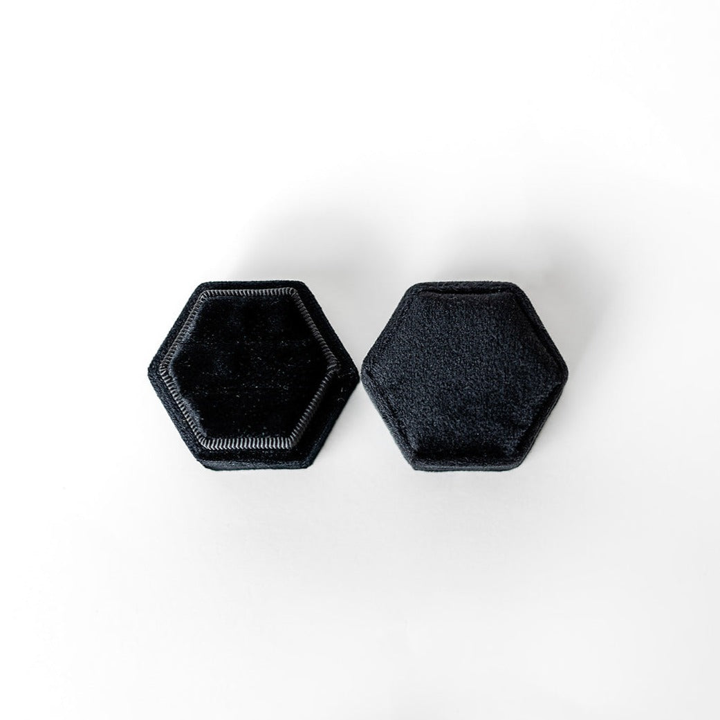 A black hexagon ring box lays open displaying the two ring slots in the base. 