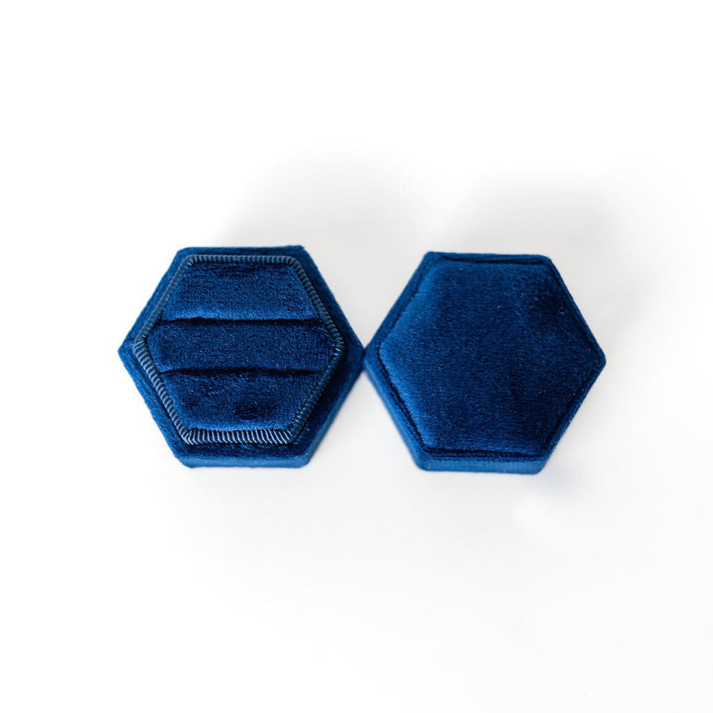 A sapphire hexagon ring box lays open displaying the two ring slots in the base. 