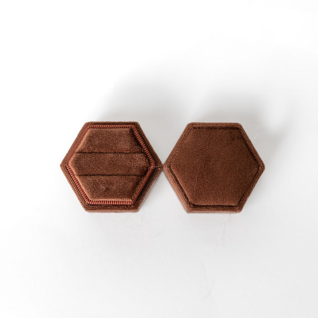 A chocolate-coloured hexagon ring box lays open displaying the two ring slots in the base. 