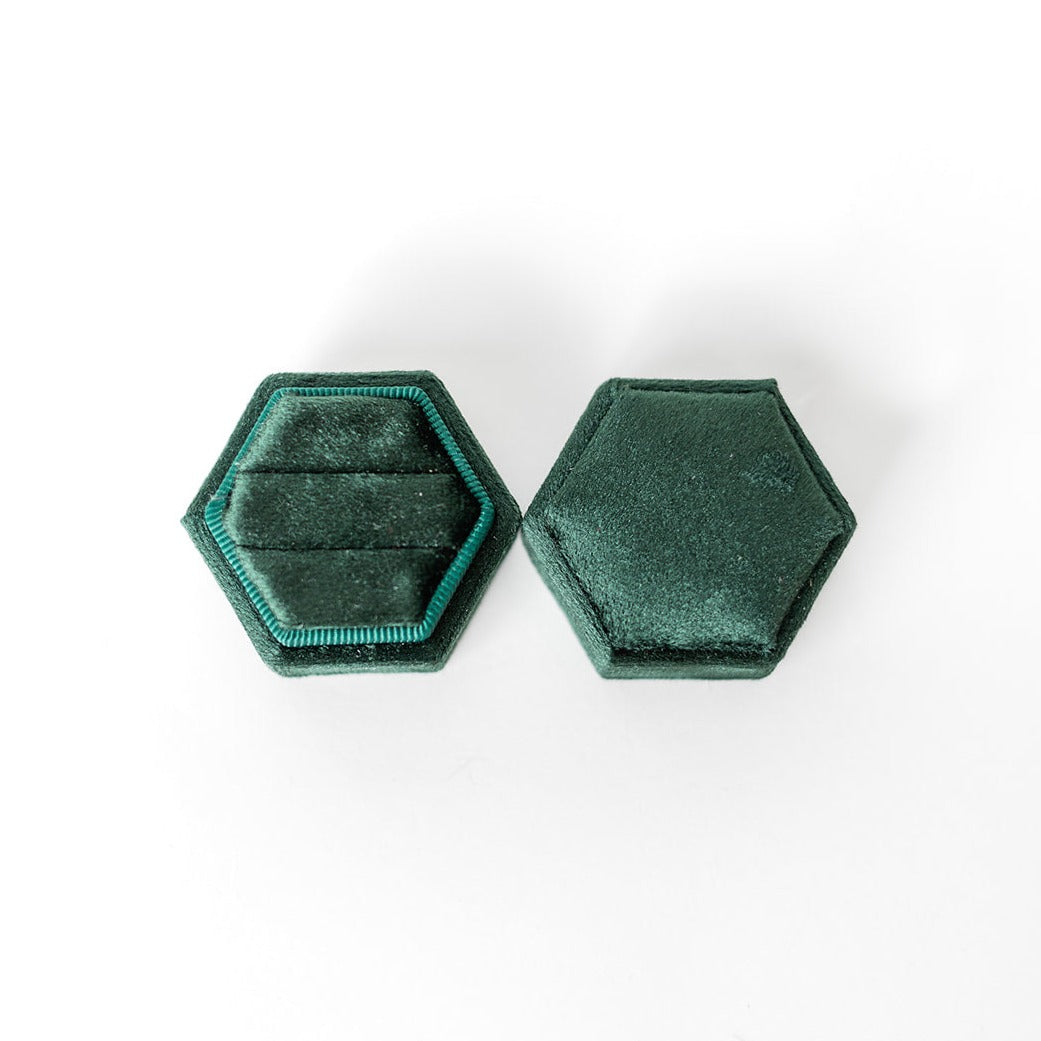 An emerald hexagon ring box lays open displaying the two ring slots in the base. 