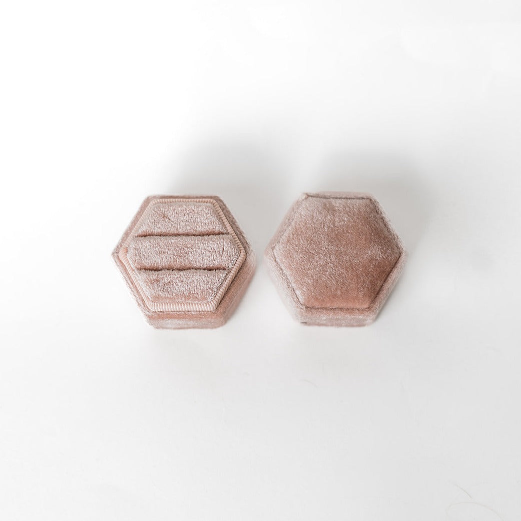 A blush-coloured hexagon ring box lays open displaying the two ring slots in the base. 