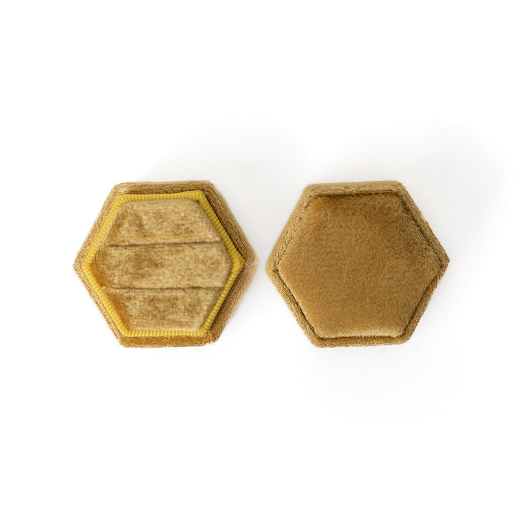 A mustard-coloured hexagon ring box lays open displaying the two ring slots in the base. 