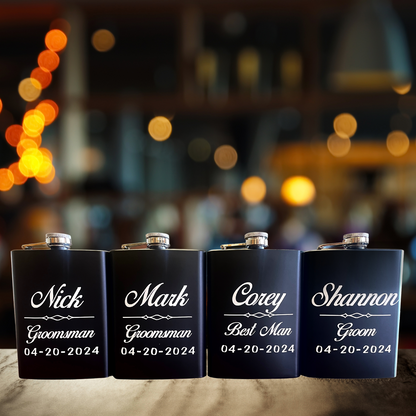 Four black flasks with white text sit on a table with bar setting in the background.