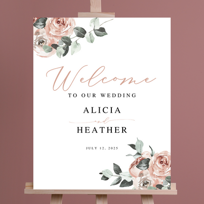 A wedding welcome sign with blush coloured florals sits on an easel against a dark pink background. 