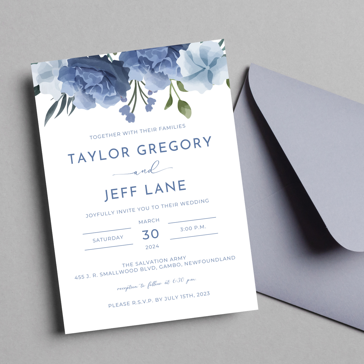 A wedding invitation with dusty blue flowers featured at the top lays on a light grey background. A blue-grey envelope is nestled underneath the invitation.
