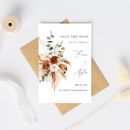 A white card with an image of a bohemian style floral bouquet sits on top of a kraft paper envelope. A spool of partially unwound white ribbon frames the card. On the Save The Date, the guest information is positioned on the right hand side.