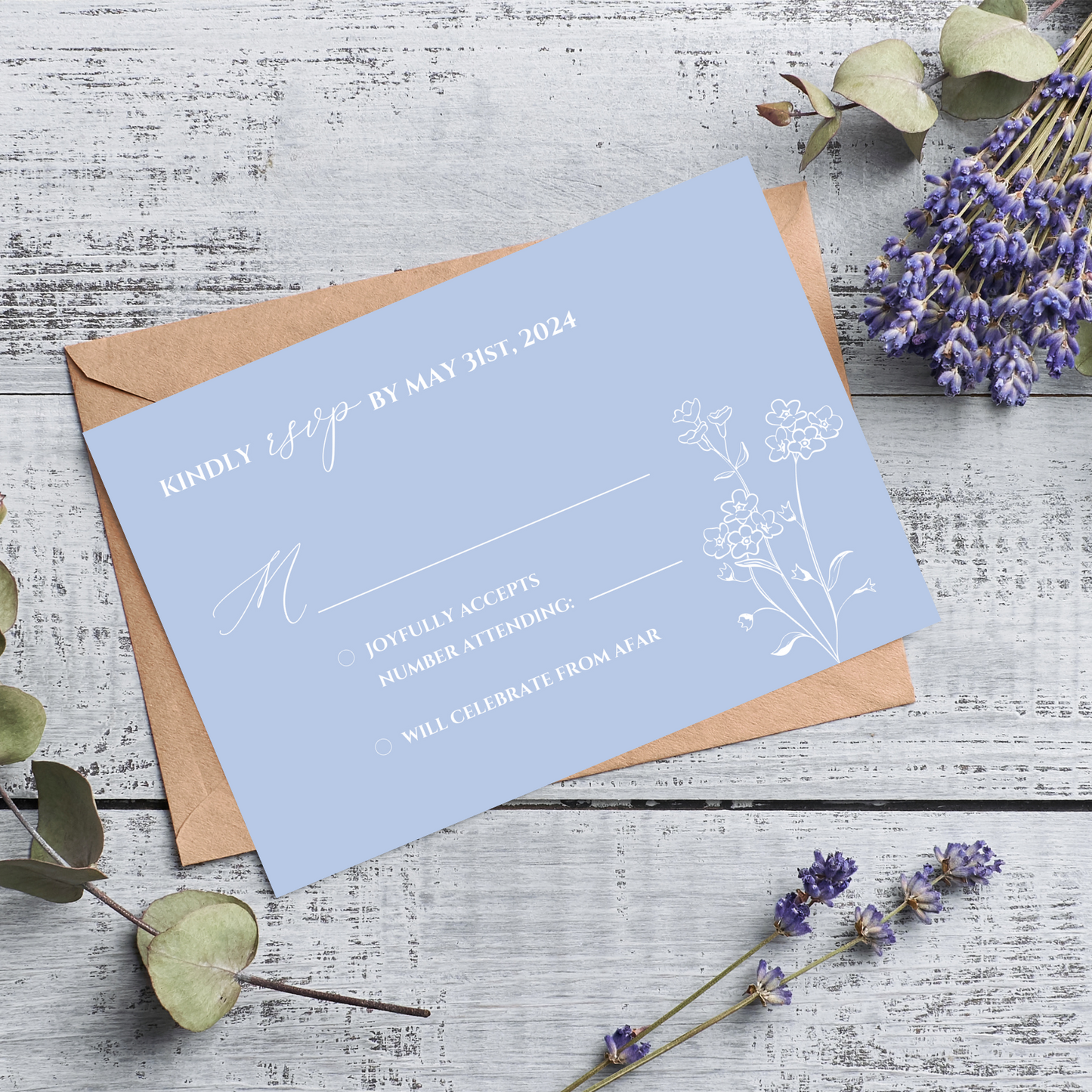 A light blue card sits on top of a kraft paper envelope against a rustic wood background. Sprigs of lilac and eucalyptus surround the card. On the R.S.V.P. itself, there is white text and a minimalist floral design. 