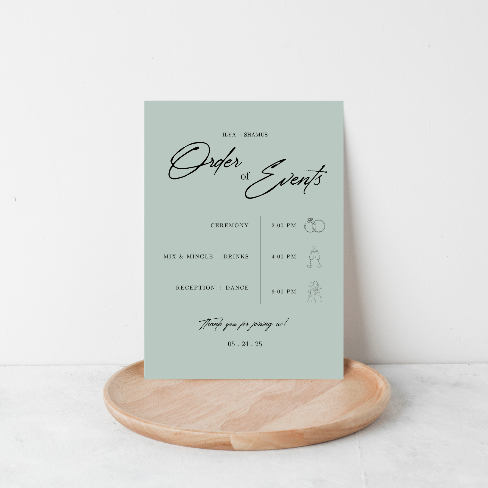 A mint green wedding program with black text stands on a light-coloured wooden plate against a white background.