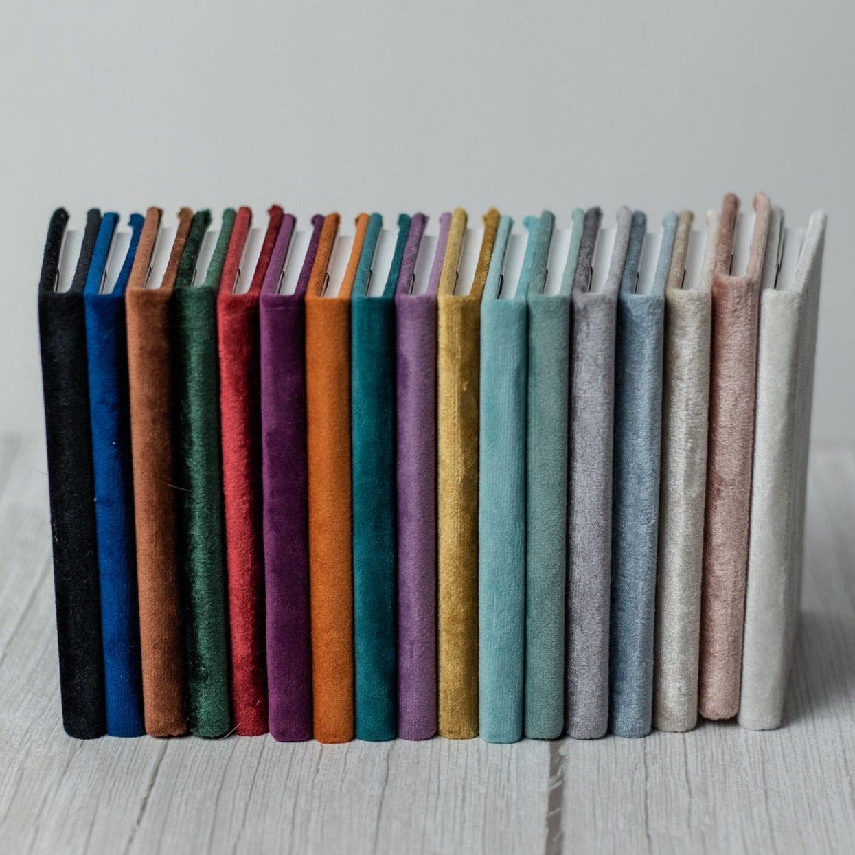 Multiple velvet vow books stand upright in a line from the darkest shade to the lightest. 